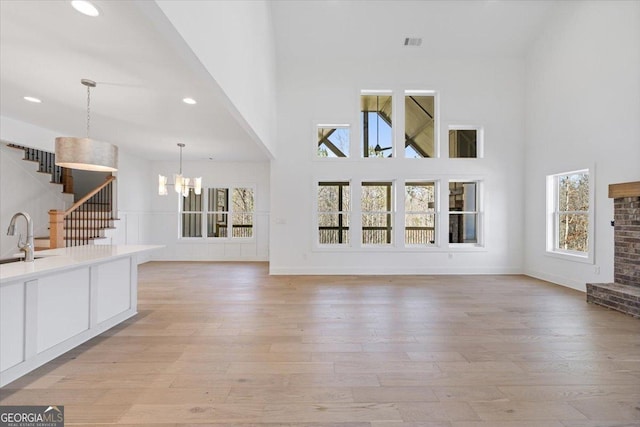 unfurnished living room featuring light wood finished floors, visible vents, stairway, a high ceiling, and a notable chandelier