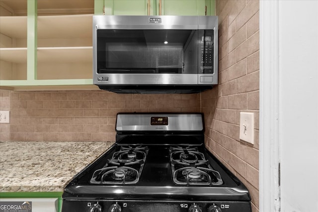 kitchen featuring black gas range, green cabinets, light stone counters, and tasteful backsplash