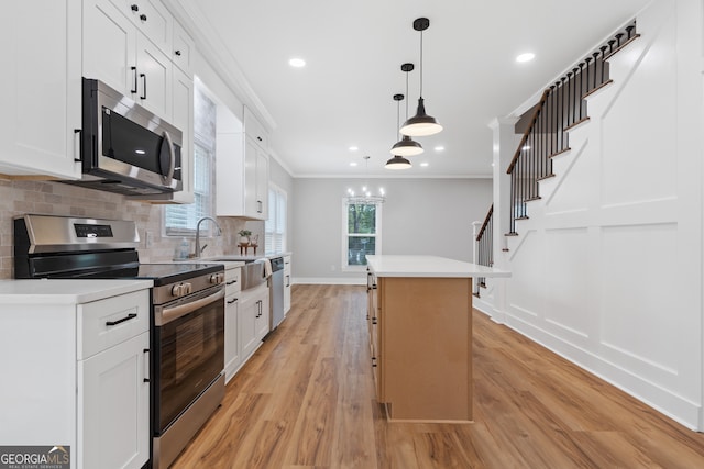 kitchen featuring white cabinetry, hanging light fixtures, stainless steel appliances, a kitchen island, and light wood-type flooring