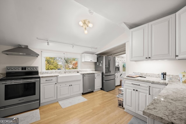 kitchen with white cabinetry, sink, stainless steel appliances, wall chimney range hood, and light hardwood / wood-style floors