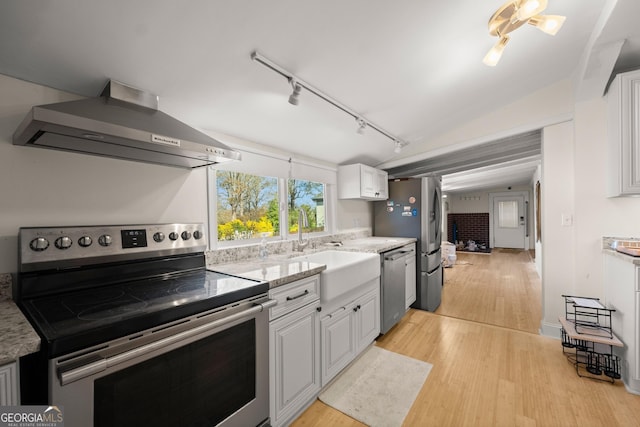 kitchen featuring white cabinets, light hardwood / wood-style flooring, vaulted ceiling, wall chimney exhaust hood, and appliances with stainless steel finishes