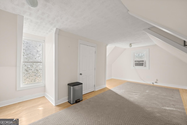 additional living space featuring a textured ceiling, light hardwood / wood-style flooring, and lofted ceiling