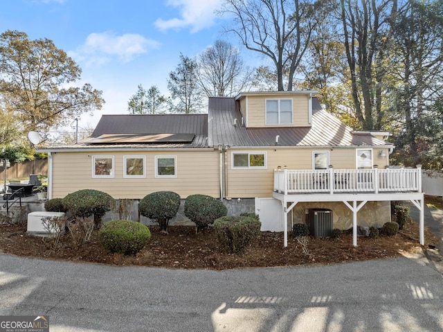 view of front of property featuring a wooden deck, cooling unit, and solar panels