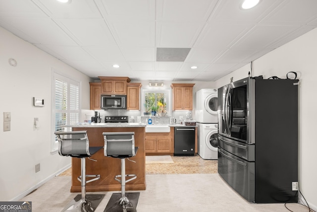 kitchen featuring a wealth of natural light, stacked washer and dryer, a kitchen bar, a kitchen island, and black appliances