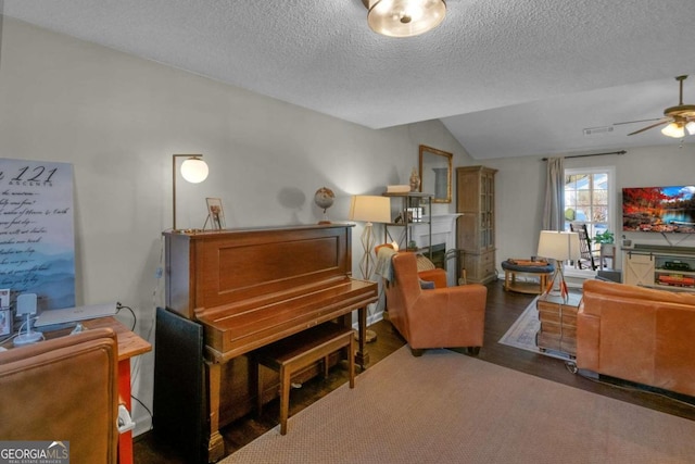 miscellaneous room featuring a textured ceiling, vaulted ceiling, ceiling fan, dark wood-type flooring, and a tiled fireplace