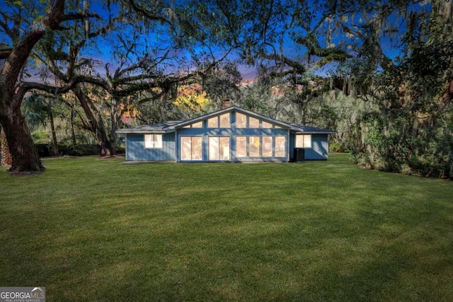 back house at dusk featuring a lawn