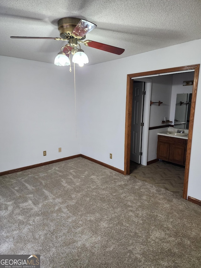 unfurnished bedroom with a ceiling fan, baseboards, a sink, a textured ceiling, and carpet flooring