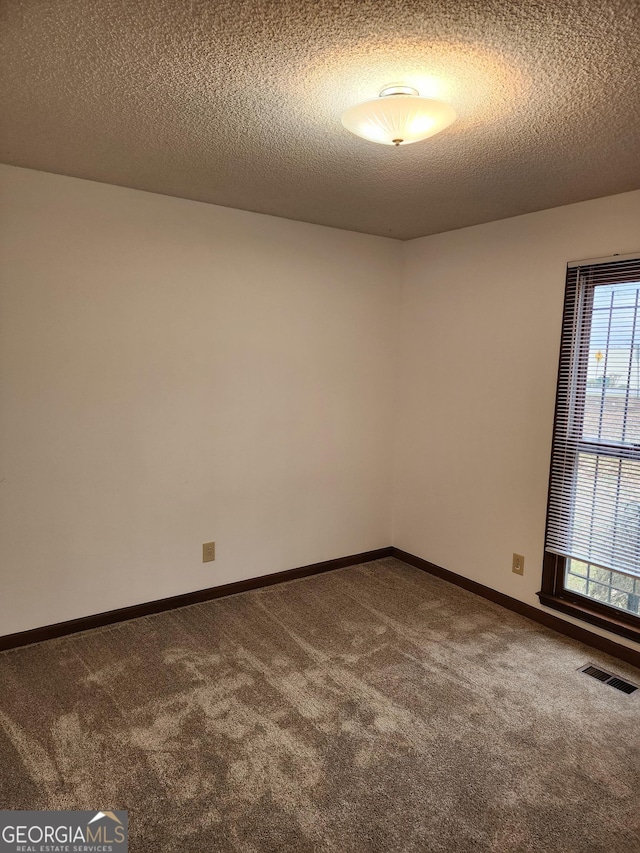 carpeted spare room featuring visible vents, a textured ceiling, and baseboards