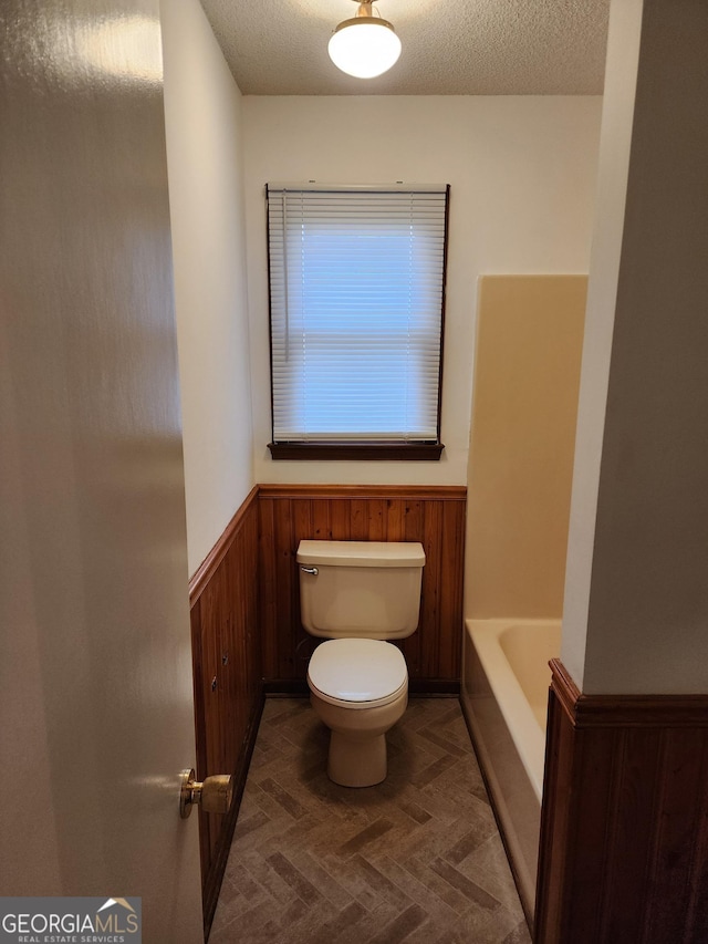 full bath featuring a wainscoted wall, toilet, wood walls, and a textured ceiling