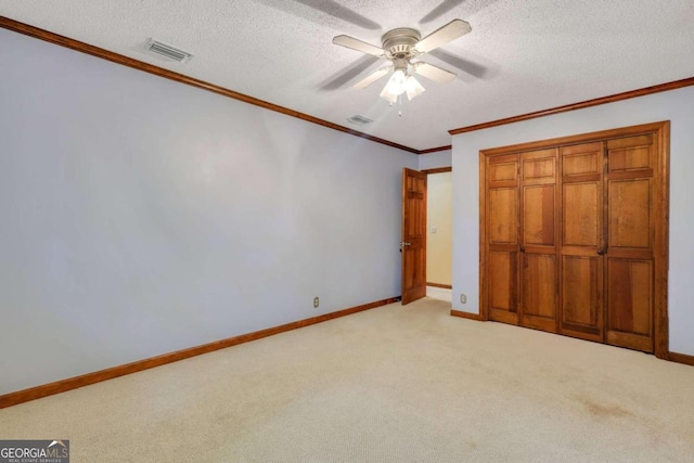 unfurnished bedroom featuring ceiling fan, a textured ceiling, light carpet, a closet, and ornamental molding