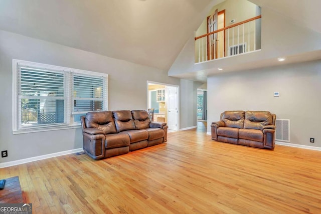 living room featuring plenty of natural light, light wood-type flooring, and high vaulted ceiling