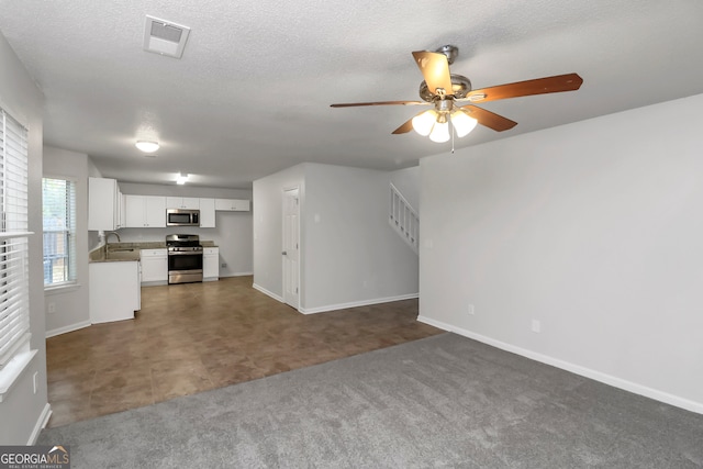 unfurnished living room with a textured ceiling, dark carpet, ceiling fan, and sink