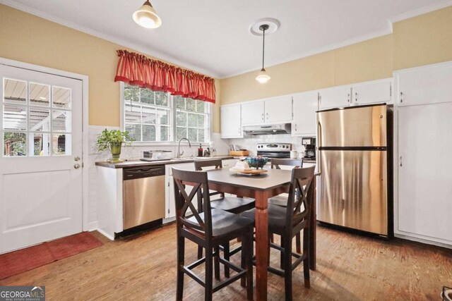 kitchen with white cabinetry, hanging light fixtures, stainless steel appliances, crown molding, and light hardwood / wood-style floors