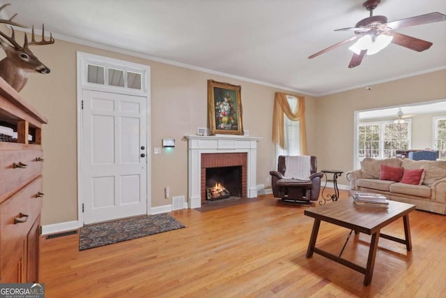 living room with a fireplace, light hardwood / wood-style floors, ceiling fan, and crown molding