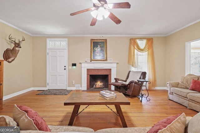 living room featuring crown molding, a fireplace, ceiling fan, and light hardwood / wood-style floors