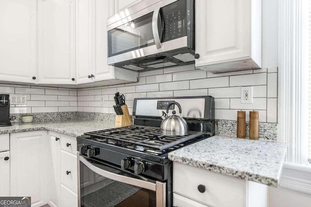 kitchen featuring stainless steel appliances, decorative backsplash, white cabinetry, and light stone countertops