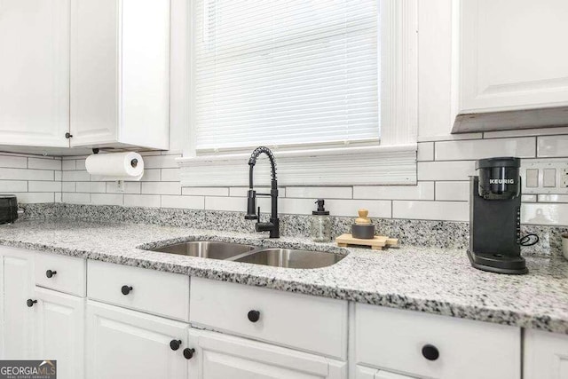 kitchen with white cabinets, backsplash, sink, and light stone counters