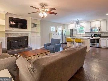 living room featuring a tile fireplace, ceiling fan, and dark wood-type flooring