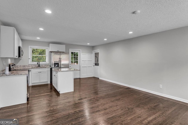 kitchen featuring appliances with stainless steel finishes, a textured ceiling, dark wood-type flooring, a center island, and white cabinetry