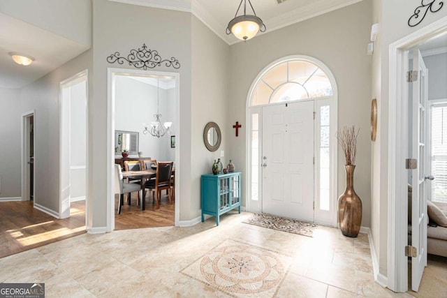 foyer entrance featuring light hardwood / wood-style flooring, a towering ceiling, crown molding, and an inviting chandelier