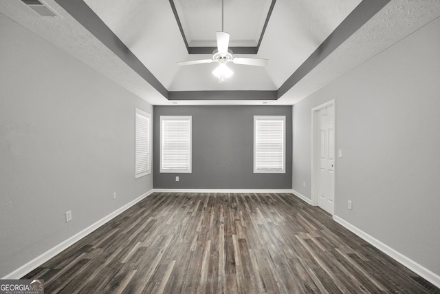 spare room with a tray ceiling, ceiling fan, and dark wood-type flooring