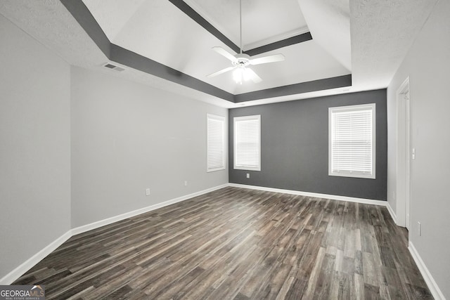 empty room with dark hardwood / wood-style flooring, ceiling fan, a raised ceiling, and a textured ceiling