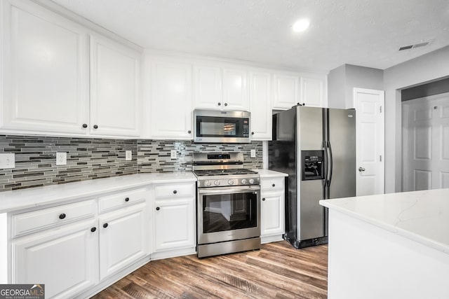 kitchen with wood-type flooring, a textured ceiling, decorative backsplash, white cabinets, and appliances with stainless steel finishes