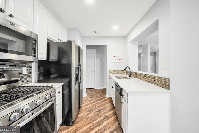 kitchen with appliances with stainless steel finishes, tasteful backsplash, sink, hardwood / wood-style flooring, and white cabinetry