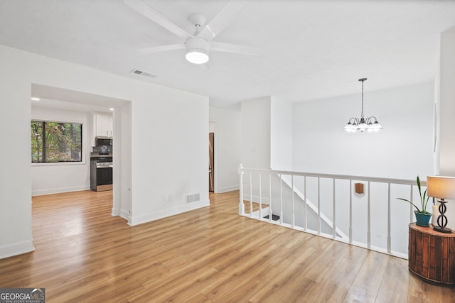 empty room with ceiling fan with notable chandelier and light wood-type flooring