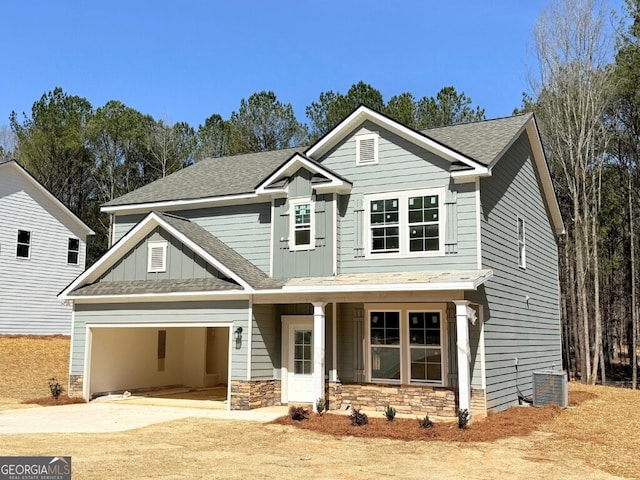 craftsman house featuring board and batten siding, a shingled roof, concrete driveway, central AC, and stone siding