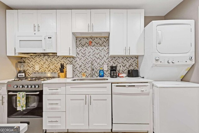 kitchen with white appliances, sink, decorative backsplash, white cabinetry, and stacked washer / dryer