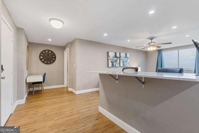 kitchen with light hardwood / wood-style floors, ceiling fan, and a breakfast bar area