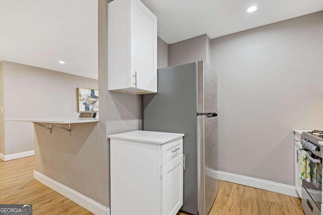 kitchen with white cabinetry, light wood-type flooring, a breakfast bar area, and appliances with stainless steel finishes