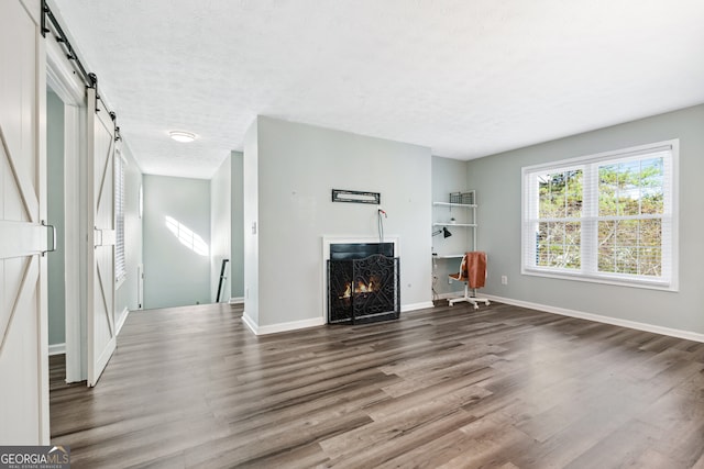 unfurnished living room featuring dark hardwood / wood-style floors, a barn door, and a textured ceiling