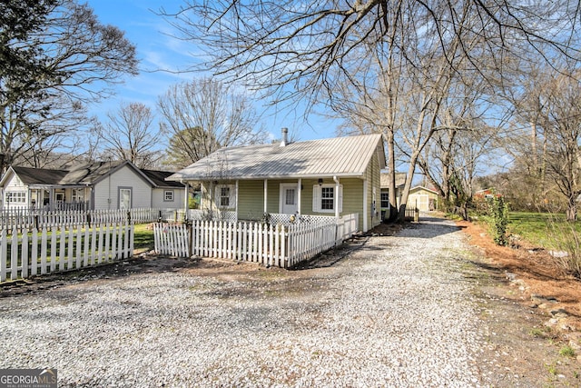 bungalow-style house featuring covered porch, metal roof, a fenced front yard, and gravel driveway