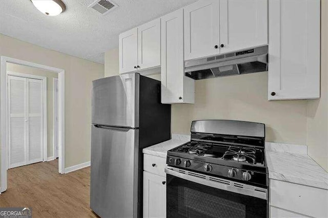 kitchen with white cabinetry, light stone counters, a textured ceiling, appliances with stainless steel finishes, and light wood-type flooring