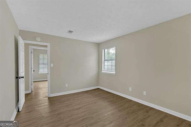 unfurnished room featuring a textured ceiling, dark hardwood / wood-style flooring, and plenty of natural light