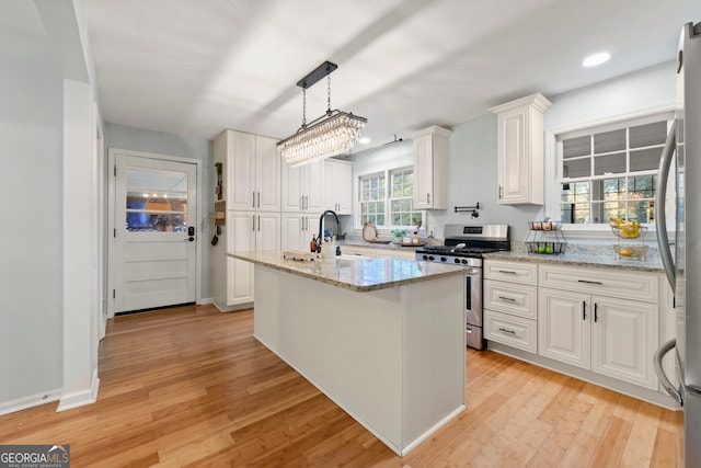 kitchen with white cabinets, a center island with sink, light wood-type flooring, light stone counters, and stainless steel appliances