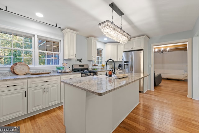 kitchen featuring hanging light fixtures, stainless steel appliances, light hardwood / wood-style flooring, a center island with sink, and white cabinets