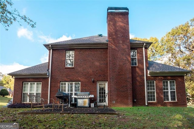 rear view of house with a patio, a yard, a chimney, and brick siding