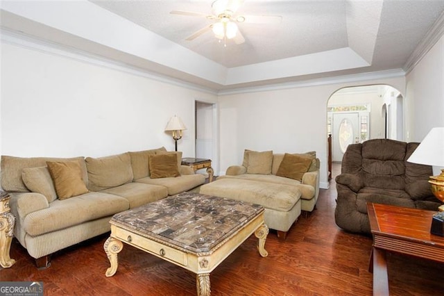 living room featuring arched walkways, crown molding, a tray ceiling, and wood finished floors