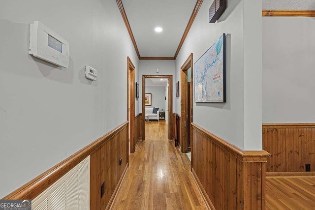 hallway with light hardwood / wood-style floors, ornamental molding, and wood walls