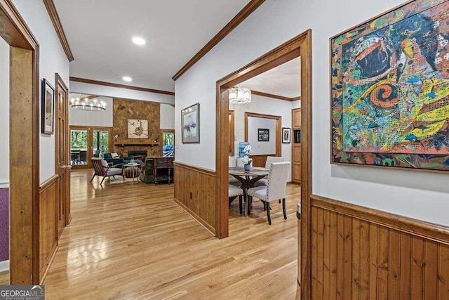 hall featuring a chandelier, light hardwood / wood-style floors, wood walls, and ornamental molding