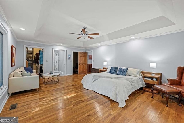 bedroom with light wood-type flooring, a walk in closet, a raised ceiling, and ceiling fan