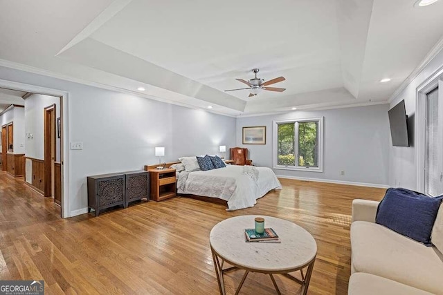 bedroom featuring light wood-type flooring, a tray ceiling, ceiling fan, and ornamental molding