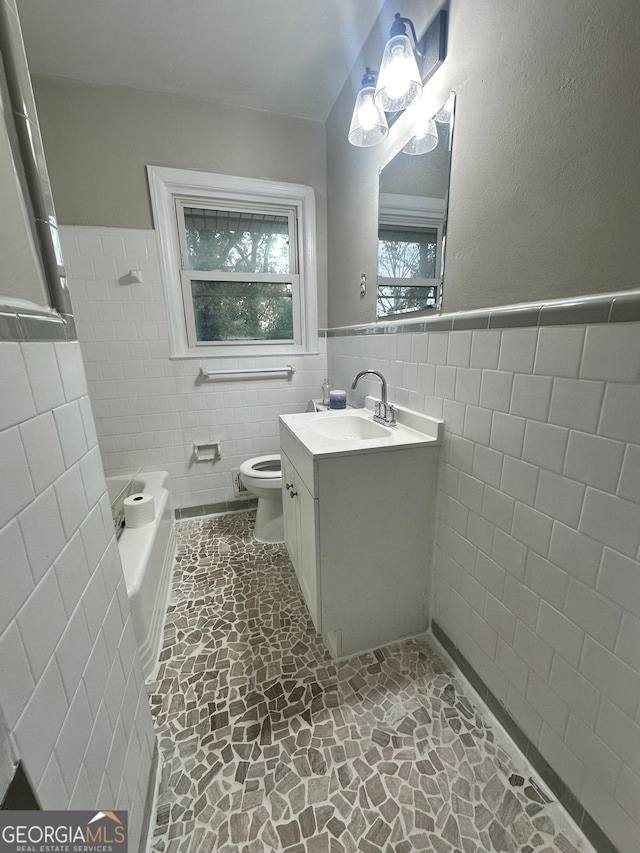 bathroom with vanity, a bath, toilet, and tile walls