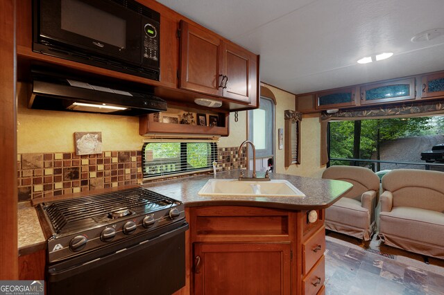 kitchen featuring kitchen peninsula, decorative backsplash, sink, and black appliances