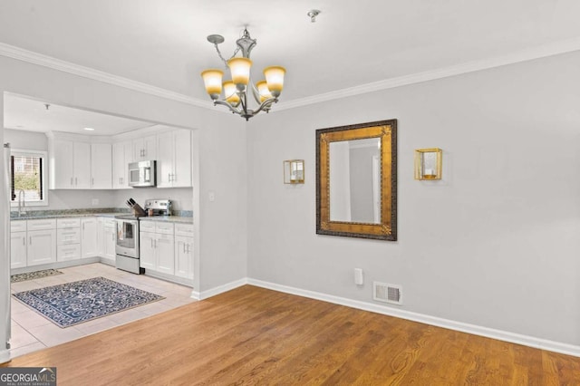 kitchen featuring white cabinets, pendant lighting, appliances with stainless steel finishes, and light hardwood / wood-style flooring