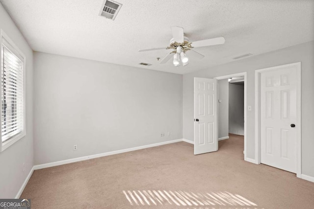 unfurnished bedroom featuring ceiling fan, light colored carpet, a textured ceiling, and multiple windows