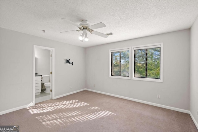 unfurnished bedroom with a textured ceiling, light colored carpet, ensuite bath, and ceiling fan